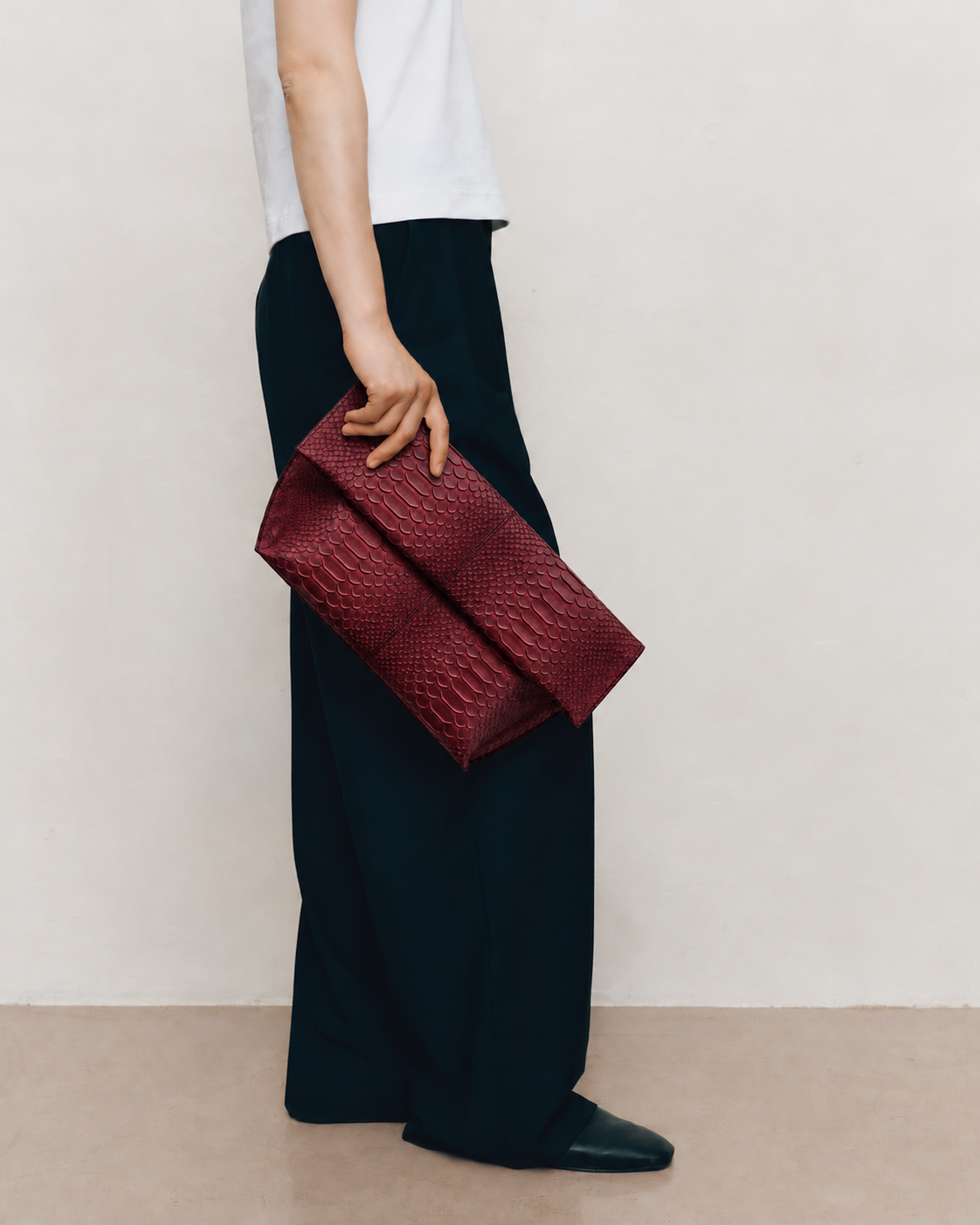 Woman carrying Deep Burgundy genuine python leather foldover clutch with minimalist outfit