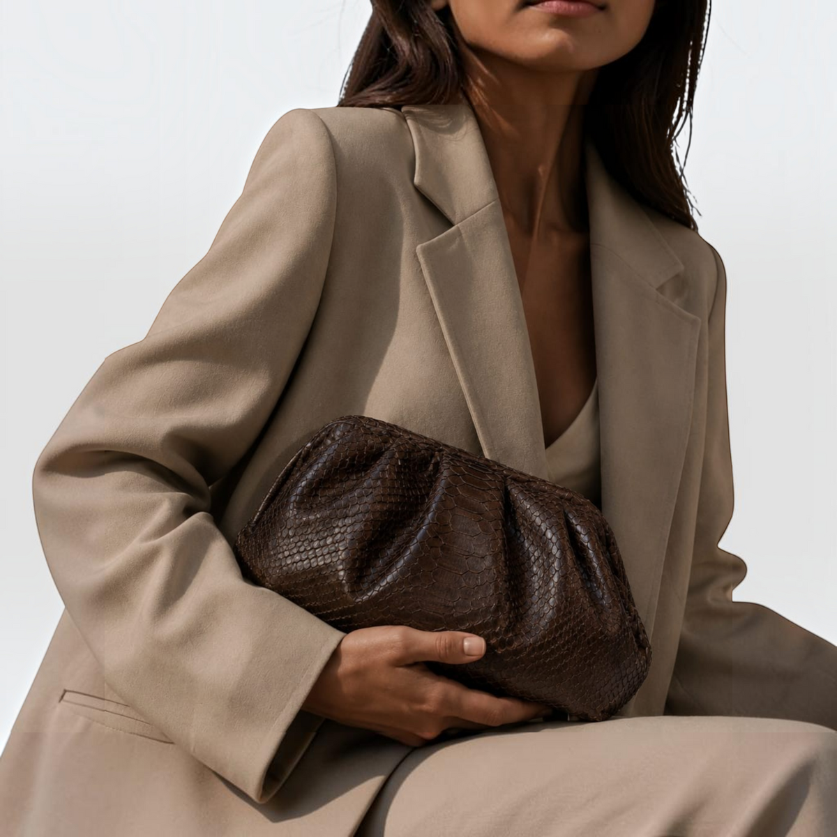 Pochette Leather craftman en cuir de python marron texturé tenue par une femme en blazer beige élégant