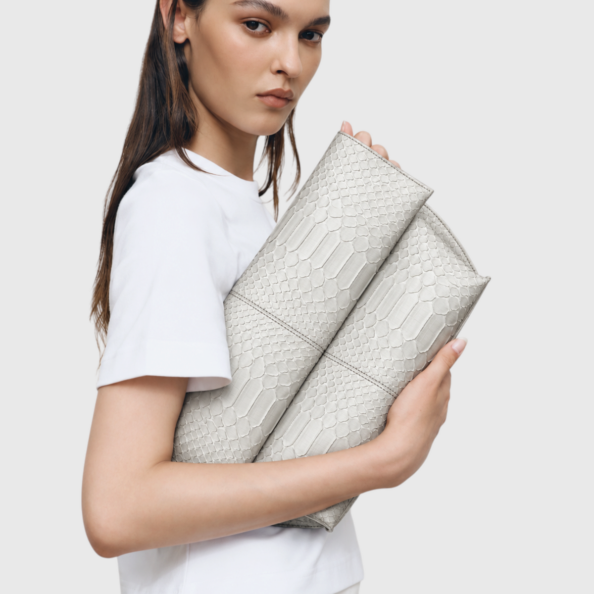 Woman holding ivory python leather foldover clutch, editorial look