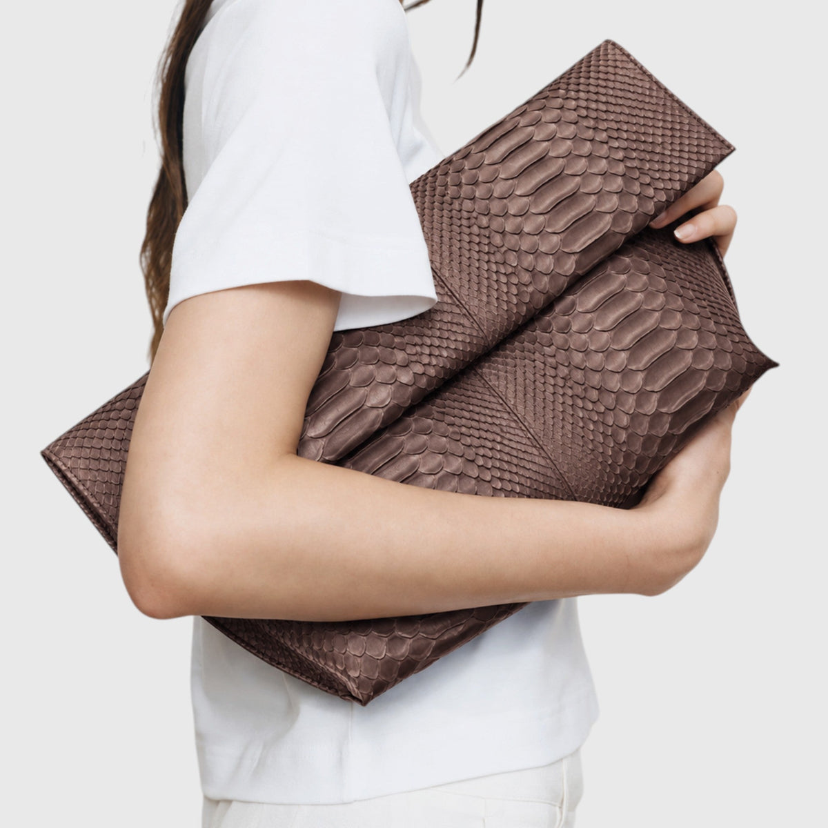 Woman holding Smoky Taupe genuine python leather clutch close-up editorial view