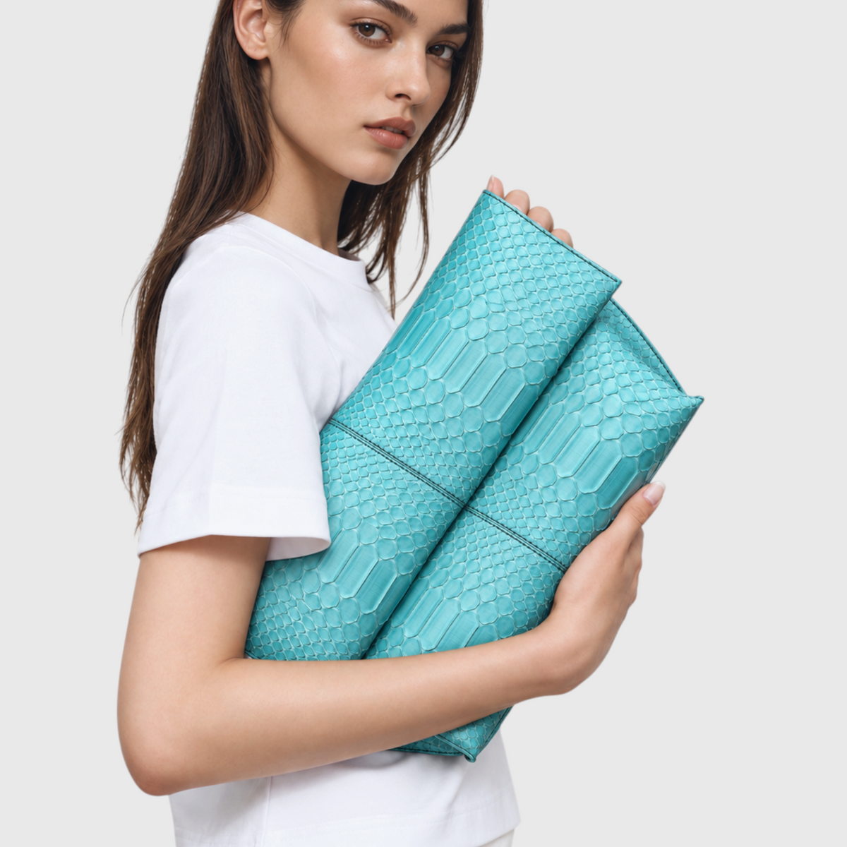 Woman holding turquoise genuine python leather foldover clutch under her arm
