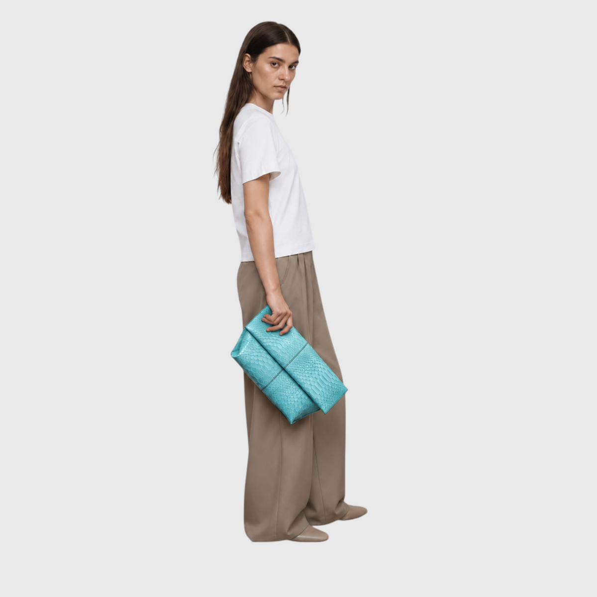 Woman carrying turquoise python leather foldover clutch with a white shirt and beige trousers