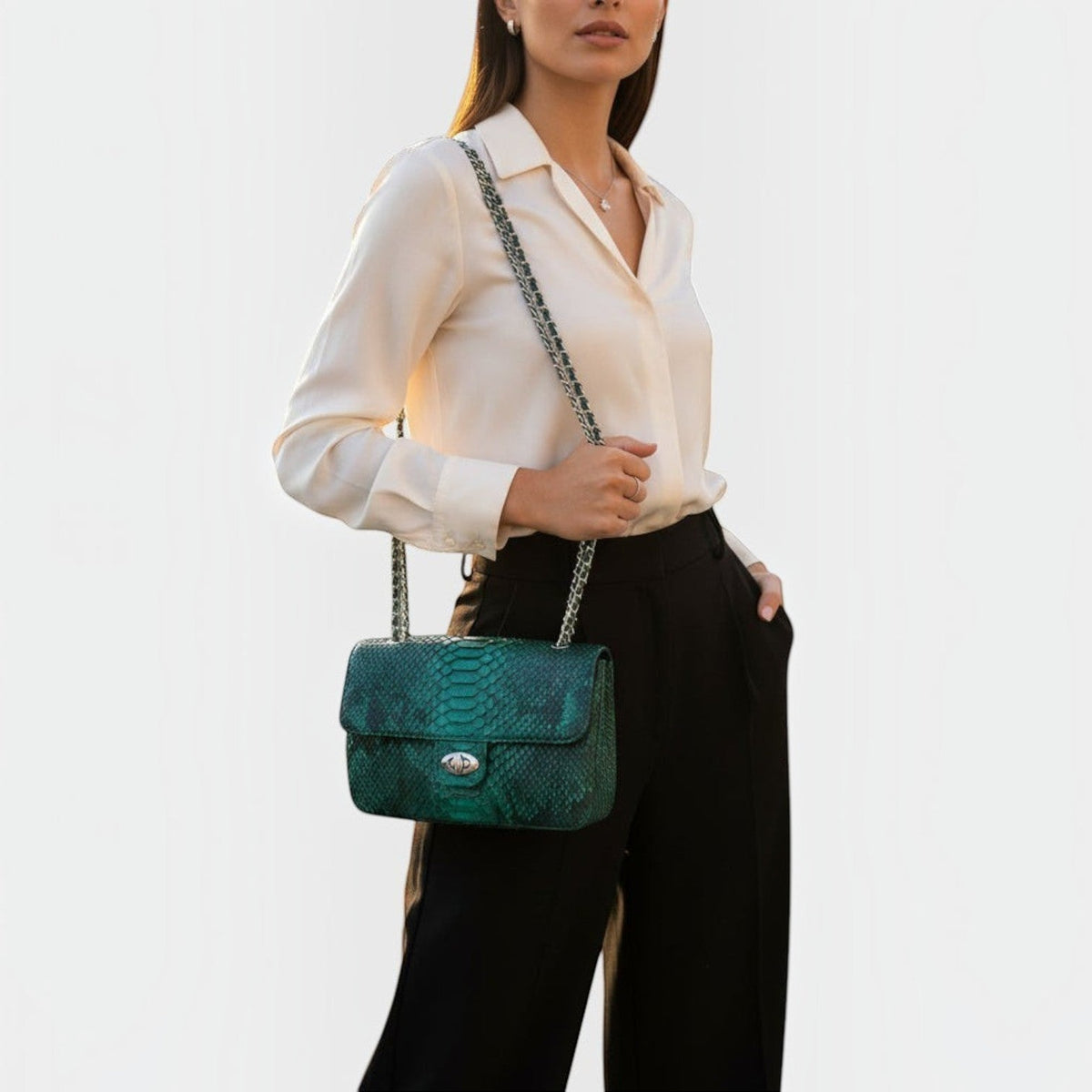 Sac à bandoulière Leather craftman en cuir émeraude texturé python avec chaîne métallique portée par une femme