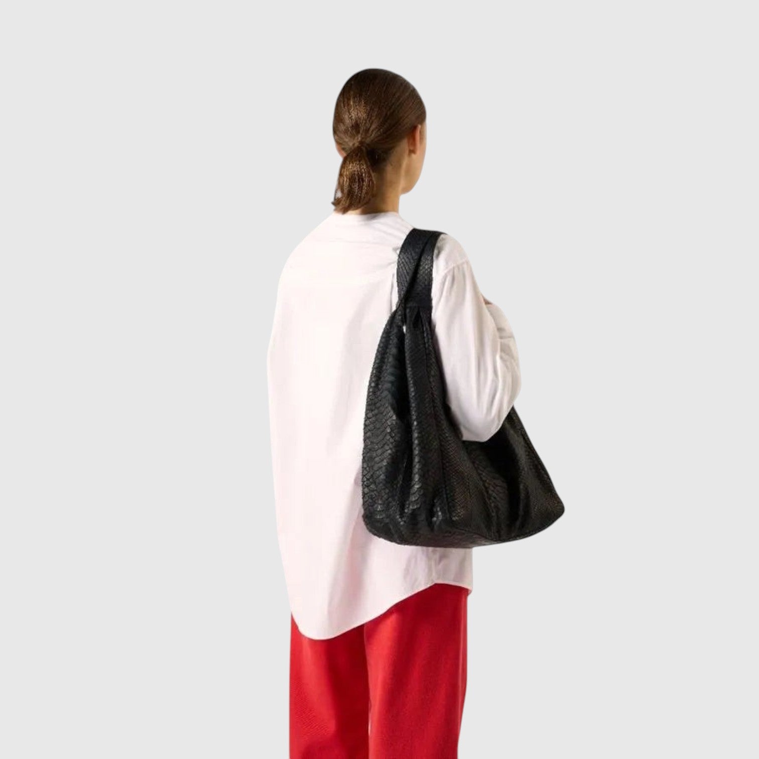 Sac hobo Leather craftman en cuir de python noir porté à l'épaule par une femme en chemise blanche