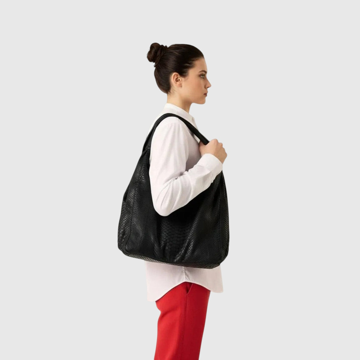 Femme portant un sac hobo Leather craftman en cuir de python noir sur l'épaule, vue de profil.