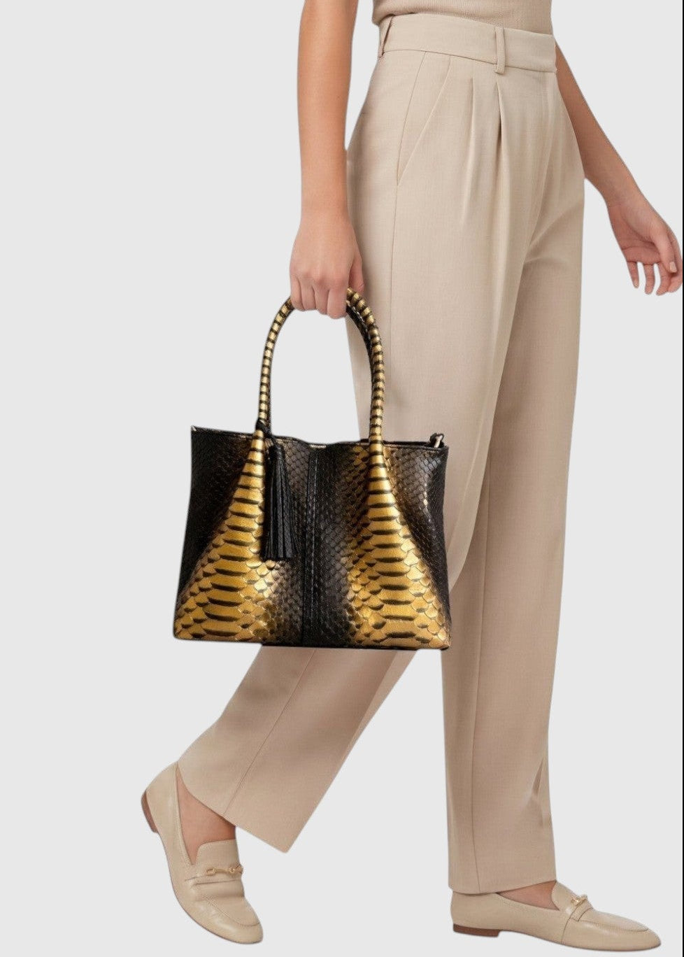 Sac à main Leather craftman en cuir de python noir et doré avec poignée structurée porté par une femme en tenue beige