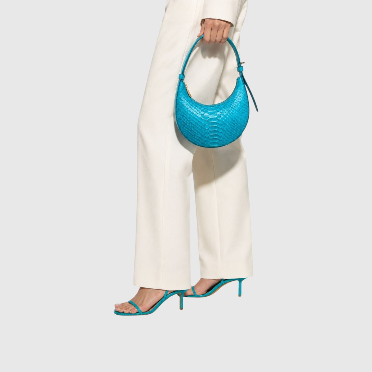 Sac à main Leather craftman bleu en cuir de python avec anse courte porté à la main par une femme en pantalon blanc