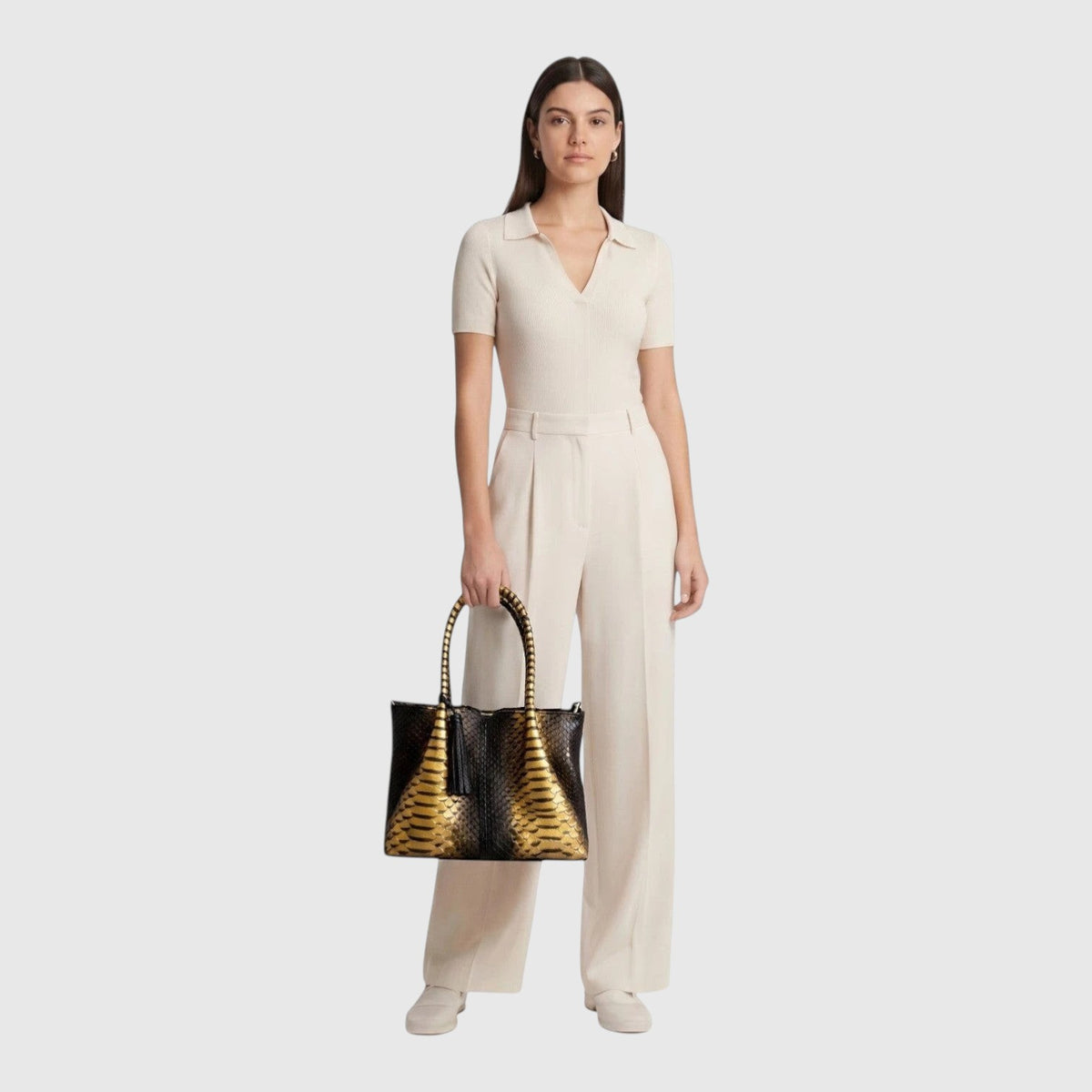 Modèle portant un sac à main structuré Leather craftman en cuir de python noir et doré avec poignée rigide
